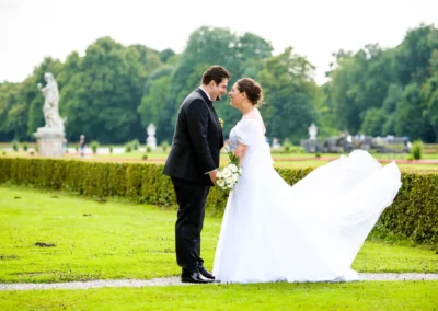 Brautpaar lacht sich an, Brautstrauss in der Hand, im Garten des Schloss Nymphenburg aufgenommen. Hochzeitsfotografie.