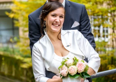 Brautpaar laechelt bei Hochzeitsportrait im englischen Garten Muenchen, Brautstrauss mit Rosen in der Hand.