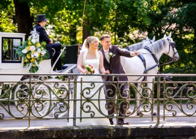 Brautpaar auf Bruecke vor Pferdekutsche im Englischen Garten Muenchen, Hochzeitsfotograf in Aktion.