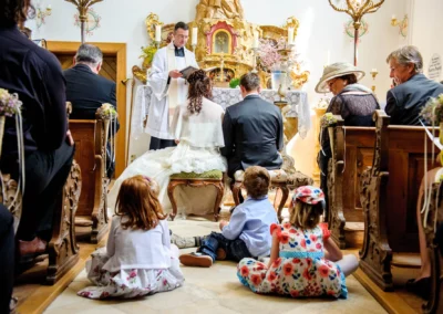 Priester leitet kirchliche Trauung im Schloss Aufhausen. Kinder sitzen am Boden; ein Teil der Hochzeitsreportage.