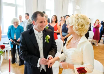 Bräutigam steckt der Braut den Ring an, umgeben von Gästen bei der standesamtlichen Trauung in Bad Toelz.