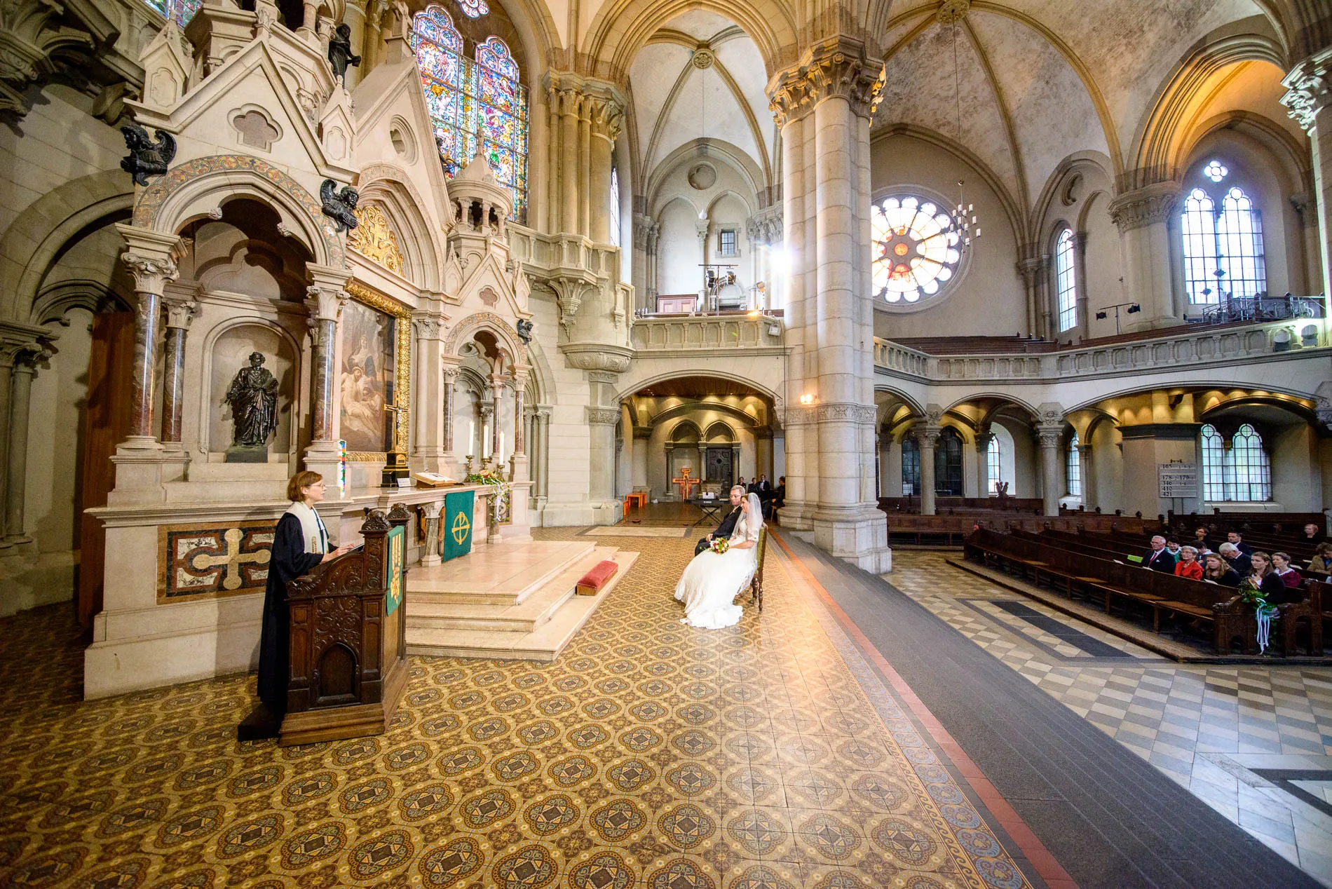 Kirchliche Trauung in St. Lukas Kirche Muenchen mit Brautpaar und Pastorin vor dem Altar, Hochzeitsfotografie.