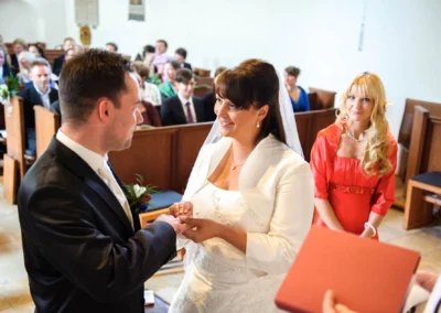 Brautpaar tauscht Ringe in Kirche bei Hochzeit nahe Muenchen, Gaeste im Hintergrund. Hochzeitsfotografie in Gauting.