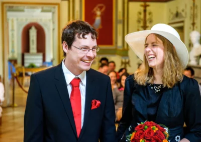 Lachendes Brautpaar bei standesamtlicher Trauung in Schloss Ismaning; Hochzeitsfoto mit Brautstrauss roter Rosen.