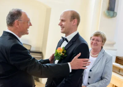 Bräutigam bei kirchlicher Trauung nahe Rosenheim, lacht mit Begleitern. Hochzeitsfoto zeigt emotionale Momente.