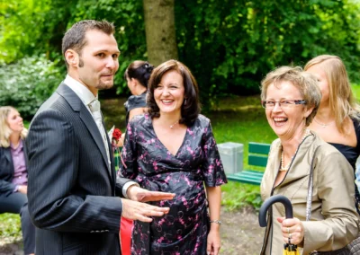 Gruppe lachender Hochzeitsgaeste im Pasinger Stadtpark bei einer kirchlichen Trauung. Hochzeitsreportage Muenchen.