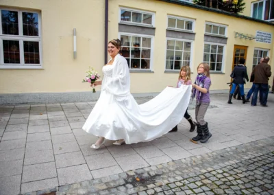 Braut in weissem Kleid bei Hochzeitsreportage, wird von zwei Maedchen begleitet, nahe Dillingen aufgenommen.