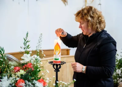 Kerze wird bei Hochzeitsfeier am Starnberger See entzündet. Dekorative Blumenarrangements im Vordergrund.