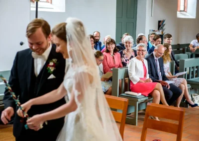 Brautpaar bei kirchlicher Trauung, Gaeste laecheln in Kirche in Ansbach, Hochzeitsfotografie.