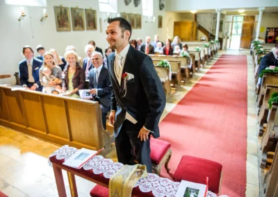 Bräutigam bei kirchlicher Trauung in München, hebt sich von der Bank, umgeben von Gästen in der Kirche.