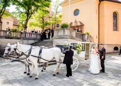 Brautpaar mit Pferdekutsche bei einer Hochzeit im englischen Garten Schwabing, Gäste im Hintergrund.