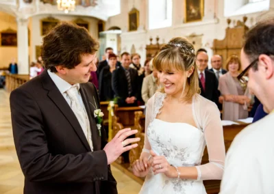 Braut und Braeutigam tauschen Ringe waehrend kirchlicher Trauung nahe Ingolstadt, umgeben von Gaesten.