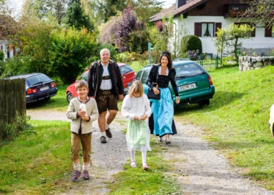 Familie in traditioneller Tracht bei einer Hochzeit nahe Starnberger See, laeuft lachend ueber einen Weg. Hochzeitsfoto.