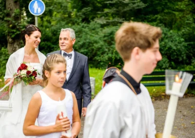 Braut mit Blumenstrauss und Begleiter bei kirchlicher Trauung im Pasinger Stadtpark, nahe München.