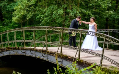 Hochzeitsfoto am Schloss Nymphenburg: Bräutigam küsst der Braut auf einer Brücke im Grünen zärtlich die Hand.