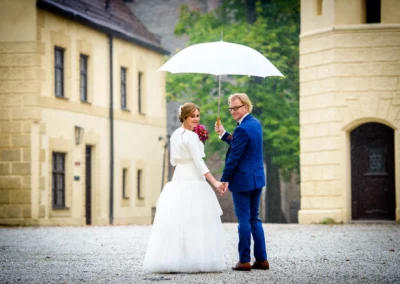 Brautpaar mit Regenschirm bei Hochzeitsfotos in Landshut. Elegantes Paar schaut zurueck zur Kamera.