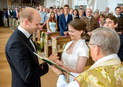 Brautpaar tauscht Ringe bei kirchlicher Trauung in St. Johann-Baptist Irschenberg vor Hochzeitsgesellschaft aus.