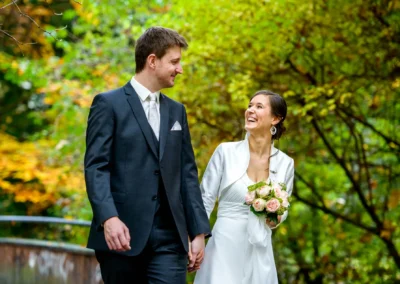 Brautpaar bei den Hochzeitsfotos im englischen Garten in Muenchen, herbstliche Baeume im Hintergrund.