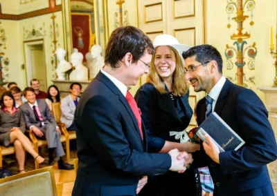 Hochzeitsfoto der standesamtlichen Trauung in Schloss Ismaning, Menschen lachen und gratulieren im prunkvollen Saal.