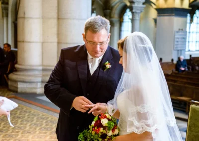 Bräutigam steckt Braut den Ring an bei kirchlicher Trauung in der Lukaskirche München, Hochzeitsfotograf in Aktion.