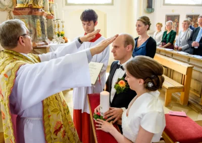 Priester segnet Brautpaar bei kirchlicher Trauung in Irschenberg, Hochzeit, Hochzeitsfotografie, Kirche im Hintergrund.