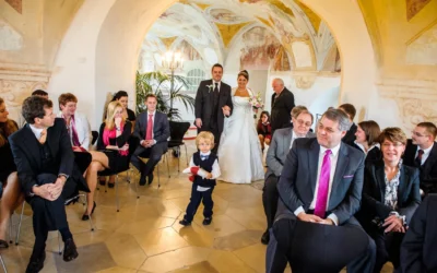 Ein Brautpaar schreitet lächelnd durch eine Bogengalerie. Hochzeitsfotografie in Schloß Höchstädt zwischen Donauwörth und Augsburg