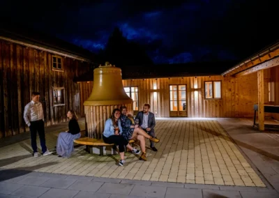 Personen sitzen auf einer Bank bei Nacht, Holzgebäude im Hintergrund. Aufnahme in Otterfing bei einer Hochzeitsreportage.