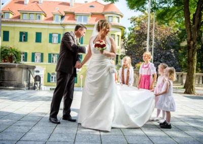 Brautpaar mit Blumenkindern vor Kirche in schwabing, Brautstrauss mit roten Rosen, Hochzeitsreportage, sonniger Tag.