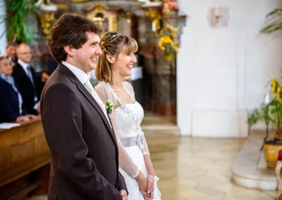 Brautpaar lacht während kirchlicher Trauung, Hochzeitsreportage nahe Ingolstadt, Blumen im Hintergrund.