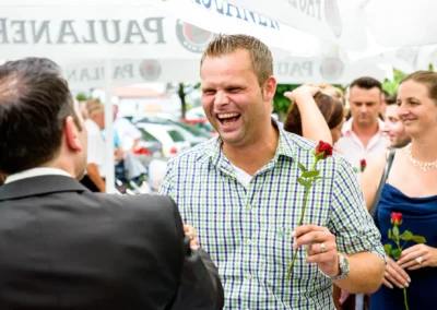 Lachende Gaeste mit Rosen bei einer Hochzeitsreportage in Roehrmoos. Feier im Freien mit Freunden.