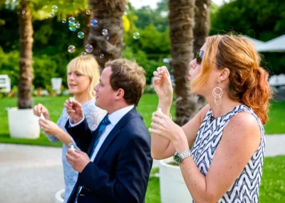 Drei Personen blasen Seifenblasen bei einer Hochzeit im Palmenhaus Schloss Nymphenburg. Hochzeitsfotografie.