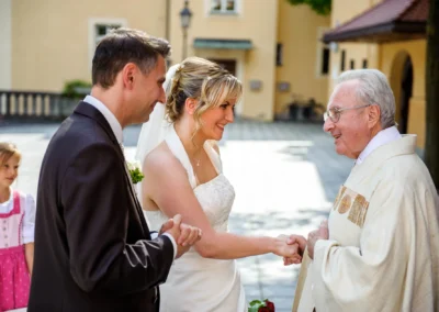 Brautpaar bei kirchlicher Trauung in München Schwabing waehrend Hochzeitsreportage mit Priester und Kind im Hintergrund.