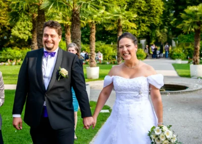 Lachendes Brautpaar spaziert Hand in Hand bei einer Hochzeit im Palmenhaus Schloss Nymphenburg, Muenchen.