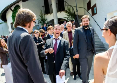 Gäste lachen bei einer Hochzeit vor der Friedenskirche Dachau. Festlicher Moment der Hochzeitsreportage.