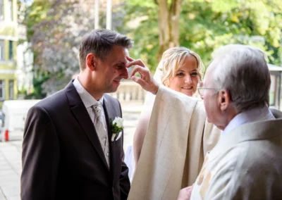 Priester segnet Brautpaar vor Kirche in Muenchen Schwabing bei ihrer kirchlichen Trauung. Hochzeitsfoto im Freien.