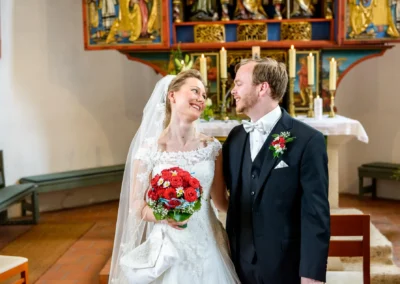 Brautpaar lacht vor Altar in Kirche, Ansbach, waehrend Hochzeitsfoto von kirchlicher Trauung gemacht wird.