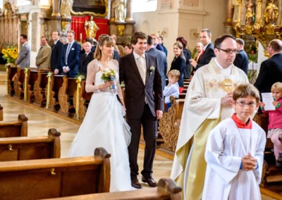 Brautpaar bei kirchlicher Trauung in Kirche nahe Ingolstadt, umgeben von Gästen und Geistlichen. Hochzeitsfoto.