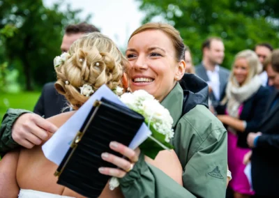 Braut umarmt Gast bei kirchlicher Trauung, Laecheln und Blumenstrauss, Hochzeitsreportage in Irschenberg.