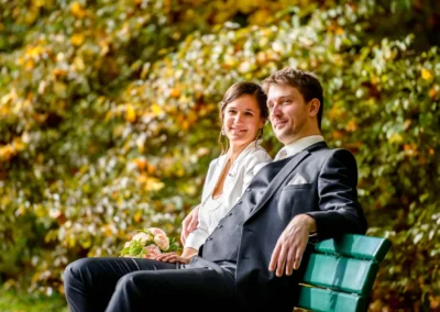 Brautpaar auf Bank im englischen Garten, herbstliche Kulisse. Hochzeitsfoto von Hochzeitsreportage in Muenchen.