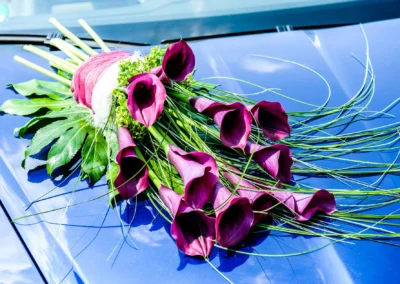 Lila Blumenstrauss auf einem blauen Auto bei einer kirchlichen Trauung in der Friedenskirche Dachau. Hochzeitsfoto.