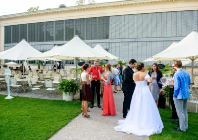 Hochzeitsfoto im Garten einer Feier im Palmenhaus Schloss Nymphenburg, Gaeste unterhalten sich unter Pavillons.