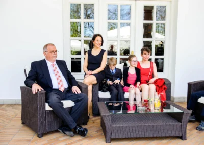 Familienportraet bei Hochzeit im Kurhaus Bad Toelz. Hochzeitsfoto zeigt Gruppe auf Terrasse bei Sonnenschein.