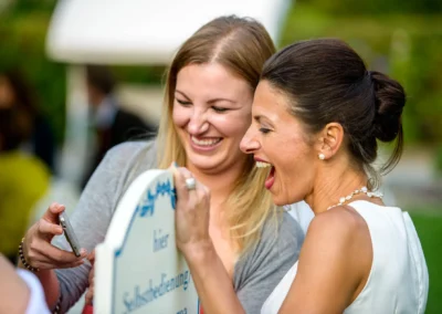 Zwei Frauen lachen bei einer Hochzeit im Freien in Nymphenburg. Hochzeitsfotografie in munchen.