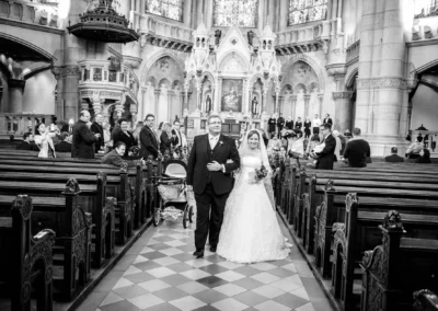 Brautpaar geht den Mittelgang der Lukaskirche in Muenchen entlang, Gaeste schauen zu, Teil der Hochzeitsfotografie.