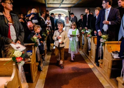 Kinder gehen den Gang einer Kirche entlang, umrahmt von Hochzeitsgaesten. Hochzeitsreportage bei Starnberger See.
