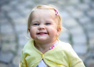 Kleines Kind in gelber Jacke laechelt bei Hochzeit in Gauting nahe Muenchen. Hochzeitsfotografie im Freien.