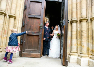 Brautpaar verlaesst Kirche St. Lukas in Muenchen, Kind streut Blumen bei Hochzeitsfoto.