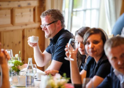 Personen sitzen bei Hochzeit an Tisch in Aschbacher Hof, trinken, lachen, Hochzeitsreportage in entspannter Atmosphare.