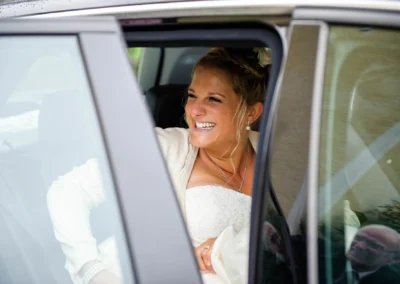 Braut strahlt beim Aussteigen aus Auto bei kirchlicher Trauung in Irschenberg, eingefangen von Hochzeitsfotograf.