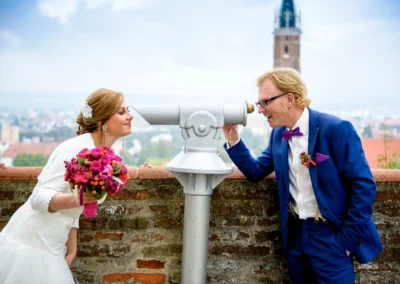 Brautpaar schaut durch ein Fernglas bei einer Hochzeitsfotografie in Landshut, Burg Trausnitz im Hintergrund.